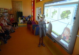 Dziewczynka wskazuje żabę z pośród innych zwierząt na prezentacji multimedialnej.